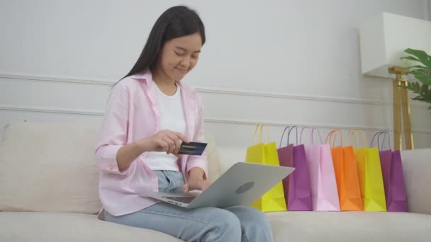 Молода азіатка, що сидить на дивані, використовуючи покупки ноутбуків онлайн з кредитною карткою, купуючи в Інтернеті, щаслива дівчина платить за транзакцію фінансову, покупку та оплату, бізнес-концепція
. - Кадри, відео