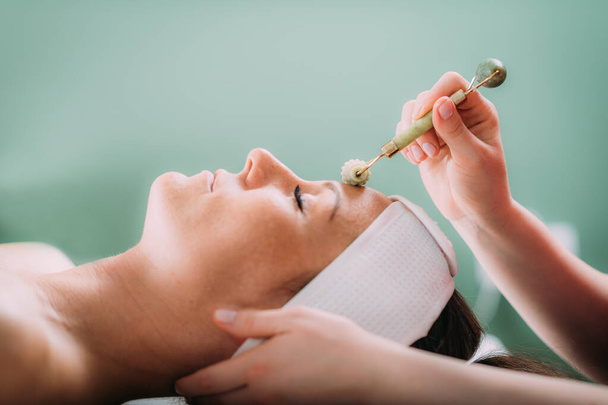 Guasha face massage in beauty salon, massage technique for stimulating pressure points on the face, using jade stone roller - Fotografie, Obrázek