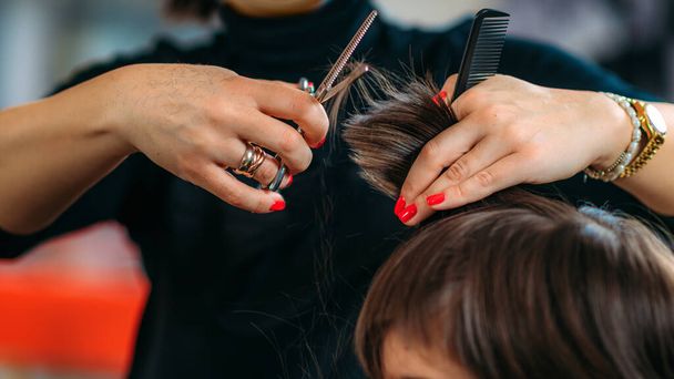 Hairdresser's hands with scissors cutting boys hair in hair salon - 写真・画像