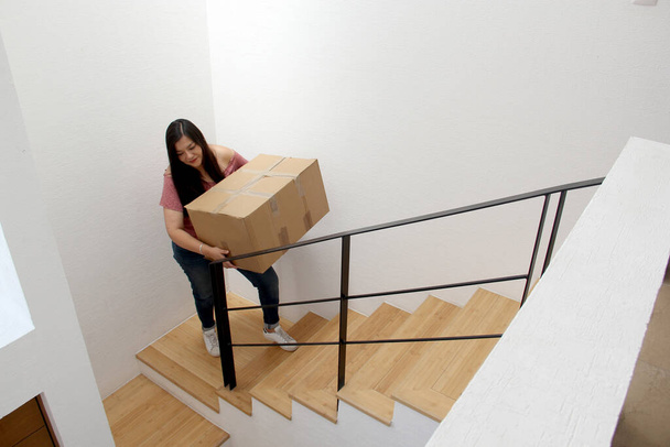Latin adult woman carries a cardboard box on the stairs of his house during a move opens house that she bought in real estate very happy for the change - Foto, Imagen