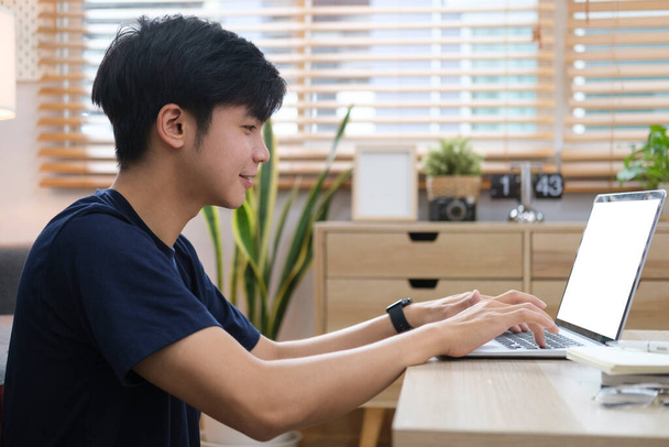 Smiling handsome asian man sitting on floor in living room and using laptop computer. - Photo, Image