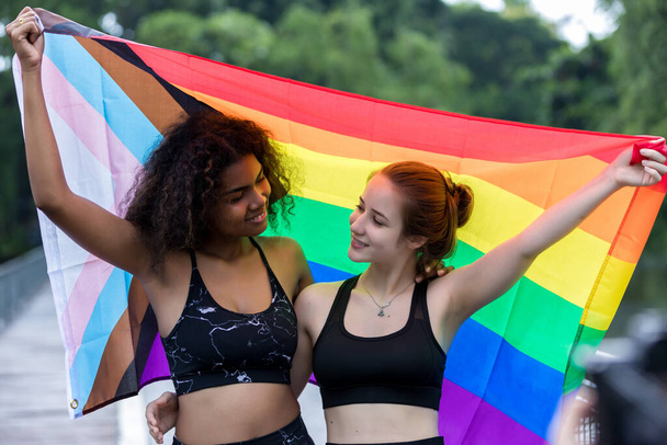Two  young women standing with a pride rainbow flag. couple hugging at outdoor. LGBT rainbow flag. - Foto, Bild