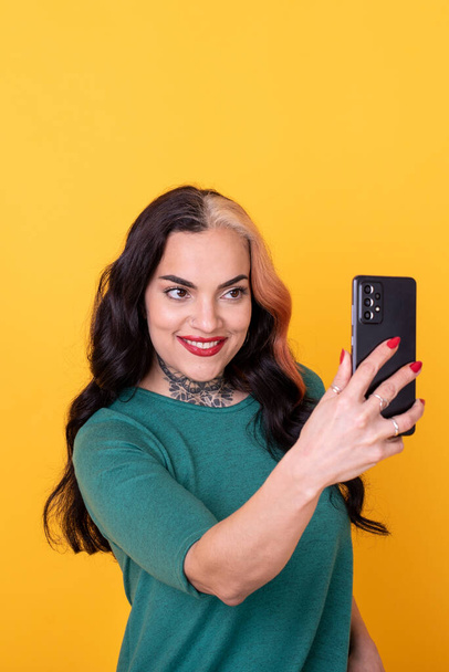 Portrait of an attractive woman making a selfie over yellow background. Studio shot. - Photo, image