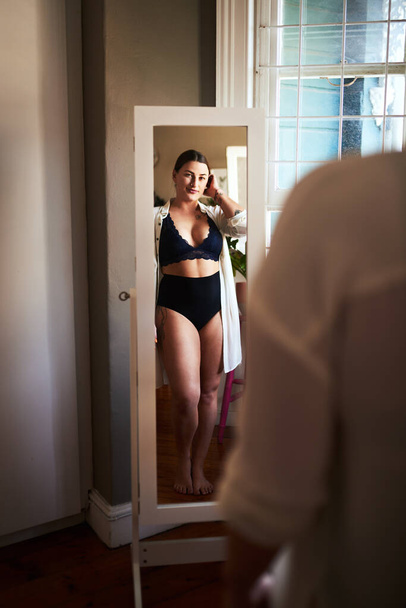Self love lives here. an attractive young woman admiring herself in the mirror in her bedroom at home - Foto, Imagem