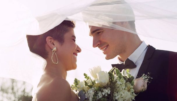Their love for each other is blossoming. an affectionate young newlywed couple smiling at each other while covering themselves with a veil on their wedding day - Foto, Bild