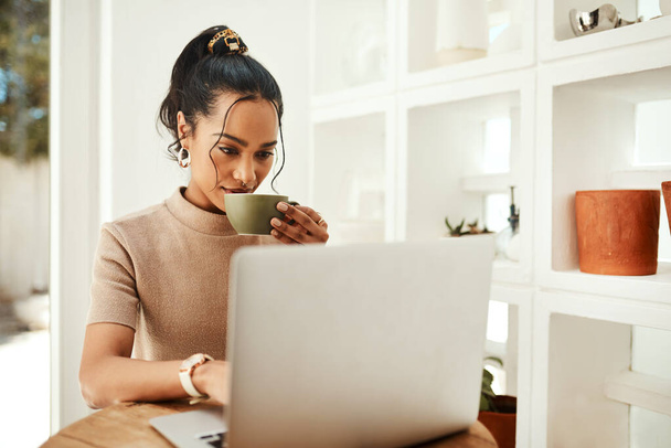 Η δουλειά των επιχειρηματιών δεν τελειώνει ποτέ. μια ελκυστική νεαρή επιχειρηματίας που κάθεται και απολαμβάνει ένα φλιτζάνι καφέ ενώ χρησιμοποιεί το laptop της στο σπίτι - Φωτογραφία, εικόνα