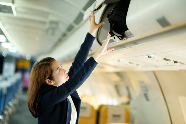 Деловая женщина кладет багаж на верхнюю полку самолета. Концепция путешествия - Фото, изображение