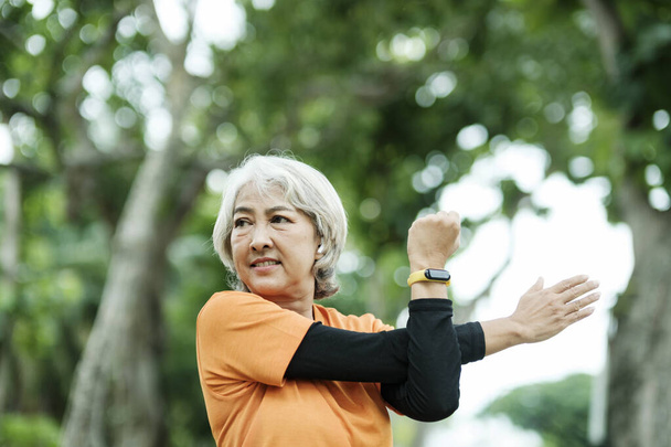 Athletic Senior woman jogger warming up by stretching arm and upper body before running in park, health concept. - Foto, afbeelding