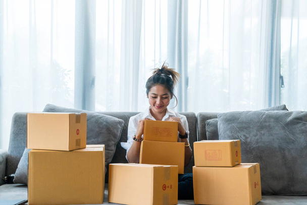 Азиатские женщины, сидящие на диване со множеством коробок с посылками с малым бизнесом, продают клиентам через интернет-магазины. Концепция продажи и покупки онлайн из дома - Фото, изображение