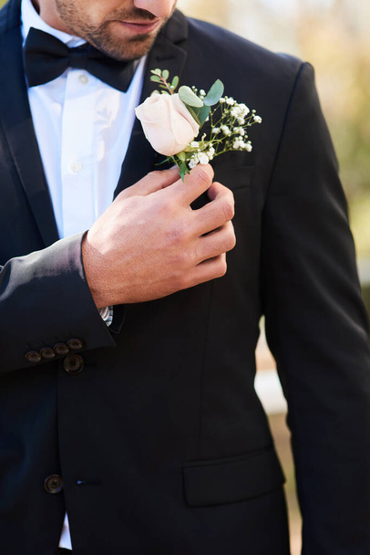 Τα λουλούδια ταιριάζουν απόλυτα σε κάθε περίσταση γιορτής. ένας αγνώριστος νεαρός γαμπρός που προσαρμόζει την μπουτονιέρα του και ετοιμάζεται να βγει έξω την ημέρα του γάμου του. - Φωτογραφία, εικόνα
