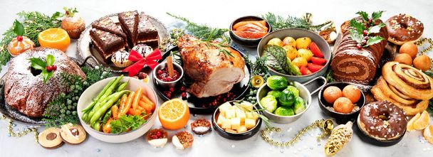 Delicious Christmas themed dinner table with roasted meat, potato, appetizers and desserts. Holiday concept. Top view on a grey background. Holiday concept. Panorama. - Foto, Bild