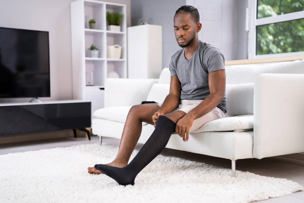 Man Putting On Medical Compression Stockings On Legs - Фото, изображение