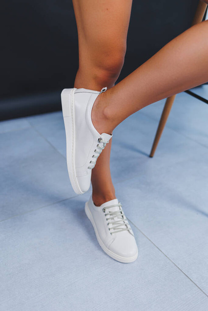 Women's legs close-up in white leather sneakers made from natural leather.Collection of women's summer shoes - Foto, Imagen