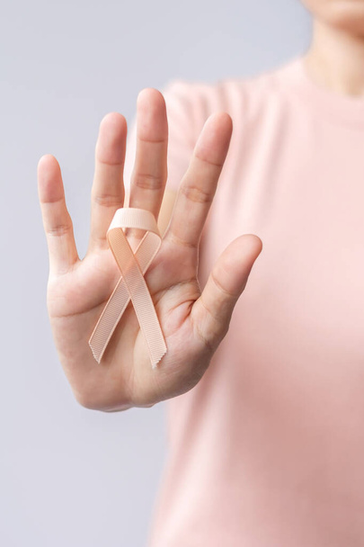 vrouw hand houden Peach Ribbon voor september Uterine Cancer Awareness maand. Gezondheidszorg en het concept van Wereldkankerdag - Foto, afbeelding