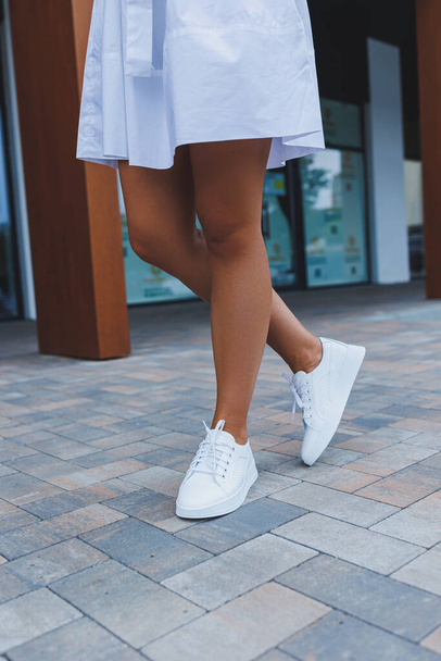 Women's legs close-up in white leather sneakers made from natural leather.Collection of women's summer shoes - Foto, imagen