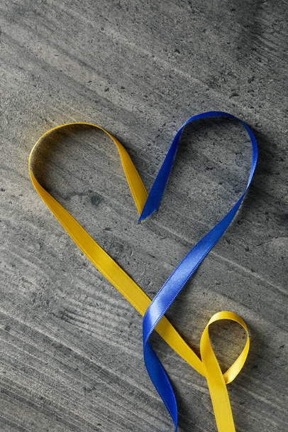 Heart made of ribbons in Ukrainian flag colors on gray wooden background - 写真・画像
