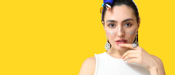 Fashionable woman with glitters on face against yellow background with space for text - Photo, Image
