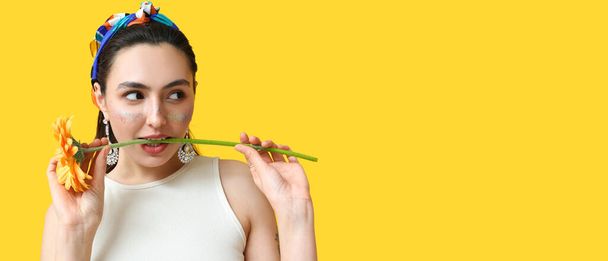 Fashionable woman with glitters on face holding flower against yellow background with space for text - Foto, Bild