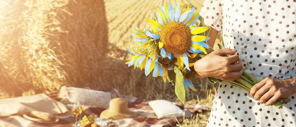 Young woman holding bouquet of sunflowers in colors of Ukrainian flag in wheat field - Photo, Image