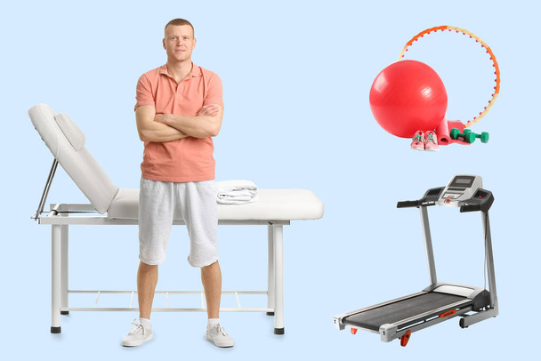 Male physiotherapist, massage couch and sports equipment on light blue background - Fotografie, Obrázek