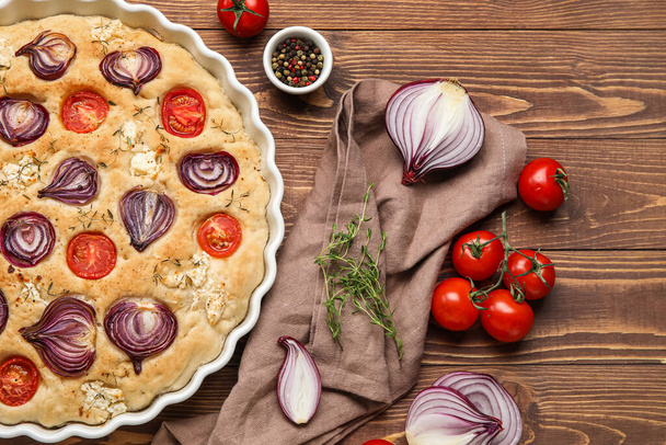 Baking dish with tasty Italian focaccia and vegetables on wooden background - Фото, изображение