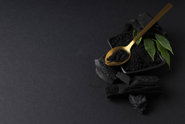 Charcoal, powdered charcoal, spoon and leaves on black background - Foto, Imagen