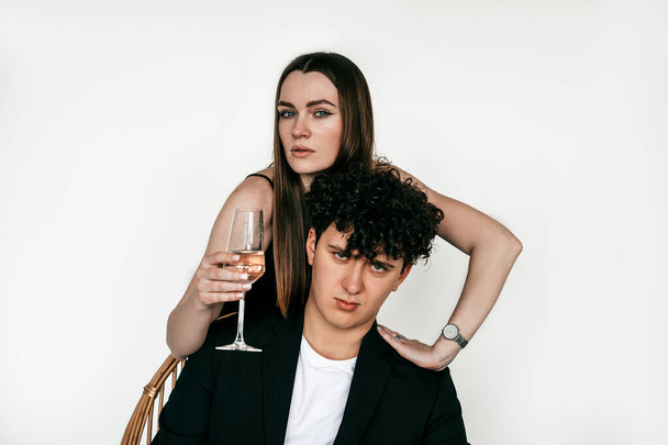 Portrait of beautiful couple in black outfits celebrating holiday with glass of champagne, gray studio background, copy space. Young girl hugging handsome boyfriend. Fashionable couples looks. - Fotoğraf, Görsel