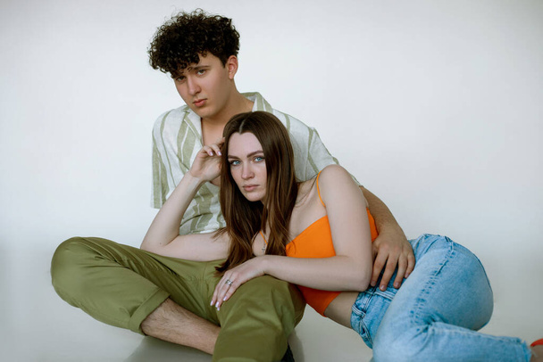 Embracing cool young couple in bright colorful summer clothes, gray studio background, copy space. Attractive girl lying on brutal guy in stylish outfit. Casual women and men wear for vacation. - Foto, Imagen