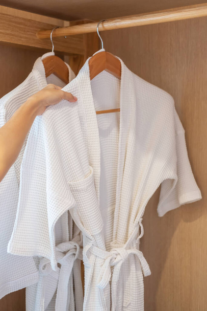 White clean bathrobe hanging in wooden wardrobe at luxury hotel or home. Relax and travel concept - Fotoğraf, Görsel
