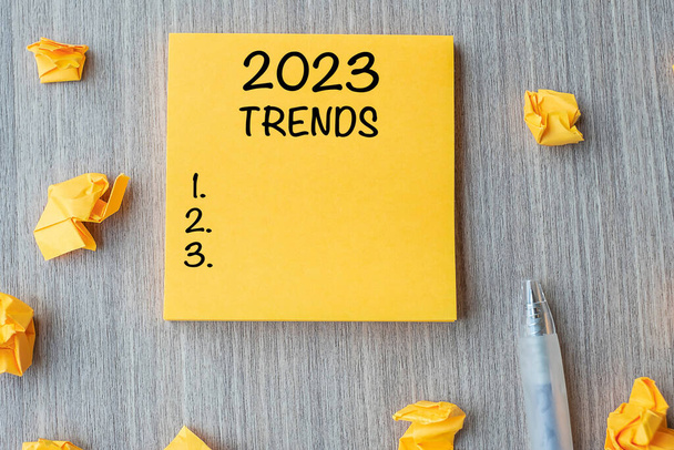 2023 Trends word on yellow note with pen and crumbled paper on wooden table background. New Year New Start, Resolutions, Strategy and Goal concept - Photo, image
