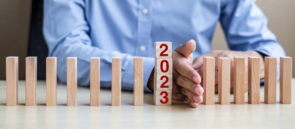 Businessman hand Stopping Falling of 2023 wooden Blocks. Business, Risk Management, Insurance, Resolution, strategy, solution, goal, New Year New You and happy holiday concepts - Fotoğraf, Görsel
