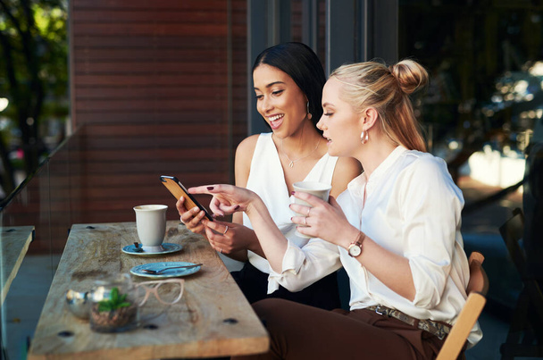 Look who just likes our picture. two young women looking at something on a cellphone while sitting at a cafe - Foto, imagen