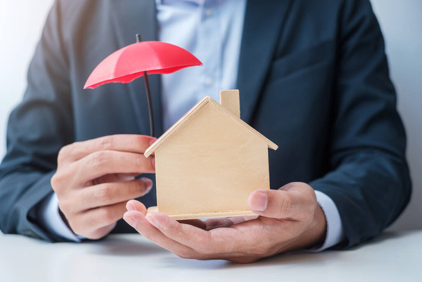 Liikemies käsi tilalla punainen sateenvarjo kansi puinen Home malli. kiinteistö-, vakuutus- ja omaisuuskäsitteet - Valokuva, kuva