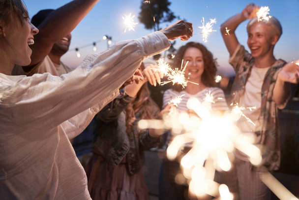 Group of friends celebrating together at the rooftop with sparkles  - Photo, Image