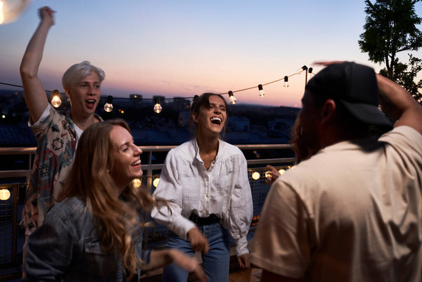 Группа счастливых друзей танцует на вечеринке на крыше                                - Фото, изображение