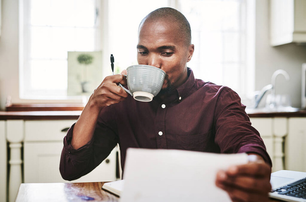 Кофеин повышает мою производительность. красивый молодой человек пьет кофе и копается в бумагах дома - Фото, изображение