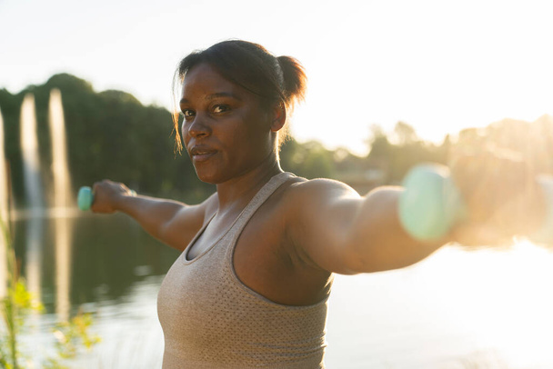 Plus sized African American woman exercising with dumbbells at the park in a  summer day - Foto, Imagem