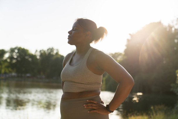 Νεαρή Αφρο-Αμερικανίδα που αναπνέει μετά από σκληρή προπόνηση στο πάρκο - Φωτογραφία, εικόνα