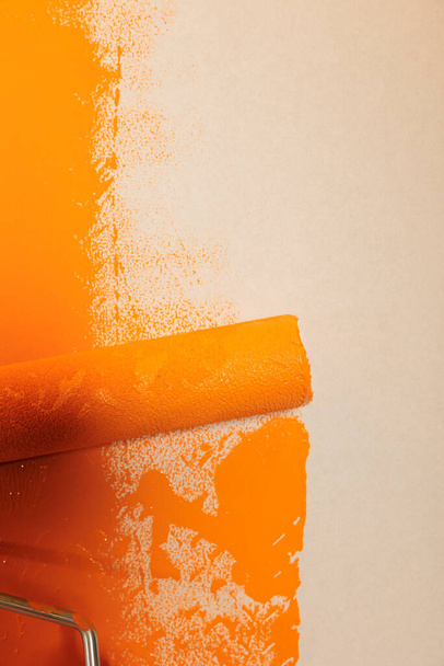 Rolling brush with orange paint to renovate and redecorate apartment walls, changing surface color with dye. Using round paintbrush with bristles and container with liquid to repaint. Close up. - Fotoğraf, Görsel