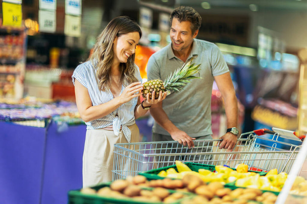 Beautiful young smiling couple choosing fruits in supermarket together - Foto, Bild