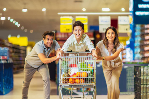 Happy family with child and shopping cart buying food at grocery store or supermarket - Photo, Image