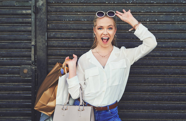 Guess what I bought today. Cropped portrait of an attractive young woman lifting her sunglasses while holding shopping bags against an urban background - 写真・画像