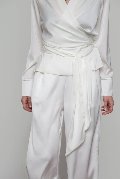 Серія студійних фотографій молодої моделі в білому класичному вбранні, блузка з шовковою атласною обгорткою та широкими ногами штанів
. - Фото, зображення
