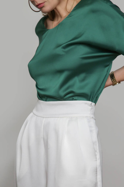 Serie of studio photos of young female model wearing emerald green silk satin batwing short sleeve blouse with white trousers. - Photo, Image