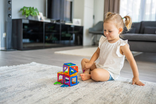 Kislány játszik színes mágnes műanyag blokkok kit otthon. A gyerek oktatási játékot játszik. Kora gyermekkori fejlődés. Kiváló minőségű fénykép - Fotó, kép