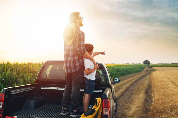 father and son standing on trunk of truck on farmland - Photo, Image