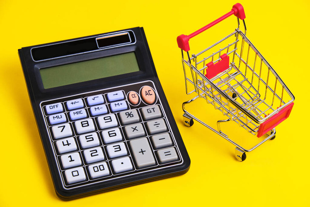 Calculator and shopping cart on yellow background.Concept of shopping and grocery shopping - Фото, зображення