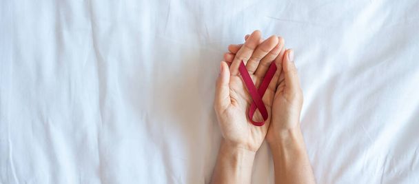 Borgoña Cinta Roja para apoyar a las personas que viven y enferman. Salud y concepto de sexo seguro. Diciembre Día Mundial del SIDA y mes de concientización sobre el cáncer del mieloma múltiple - Foto, Imagen