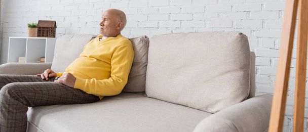 Πλευρική άποψη του συνταξιούχου κάθεται στον καναπέ στο σπίτι, πανό  - Φωτογραφία, εικόνα