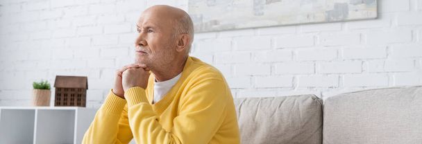 Senior man looking away while sitting on couch at home, banner  - Photo, Image